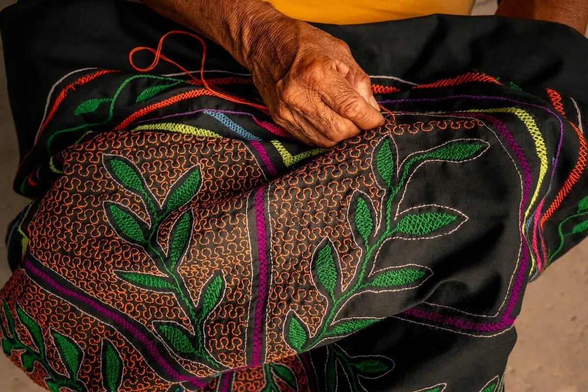 A hand stitching a Shipibo kené cloth with leaf patterns